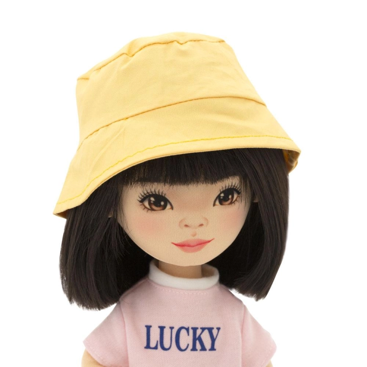 Lalka Sweet Sisters Lilu 32 cm Orange Toys, szmaciana z endoszkieletem, twarz nadrukowana cyfrowo, czarne włosy, żółty kapelusz, różowa koszulka z napisem Lucky, jasnoszare jeansy, buciki, torebka
